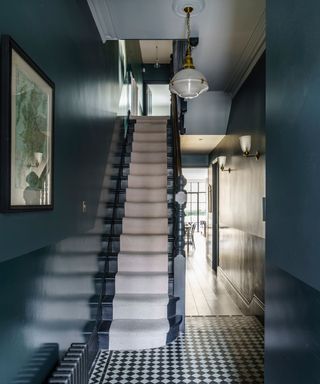 entryway in traditional Victorian home with black and white floor tiles, neutral stair runner and walls painted dark blue in gloss and matte