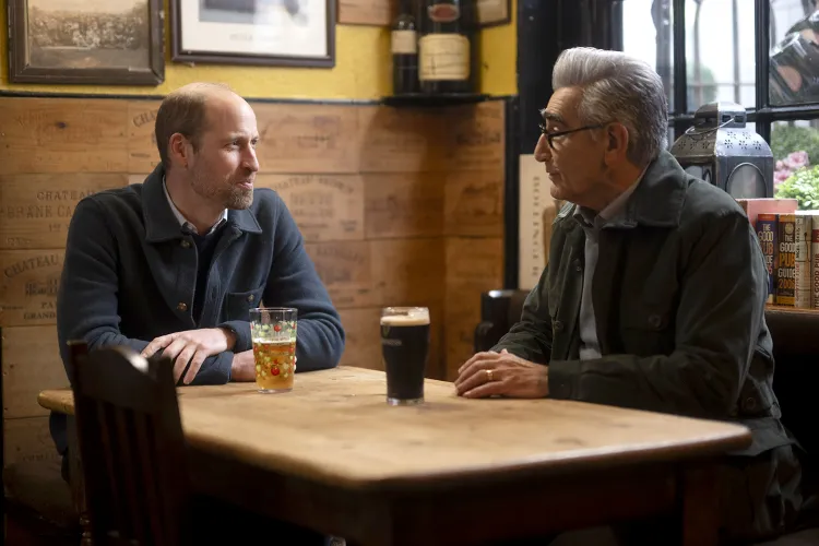 Prince William and Eugene Levy sitting at a bar table drinking beer