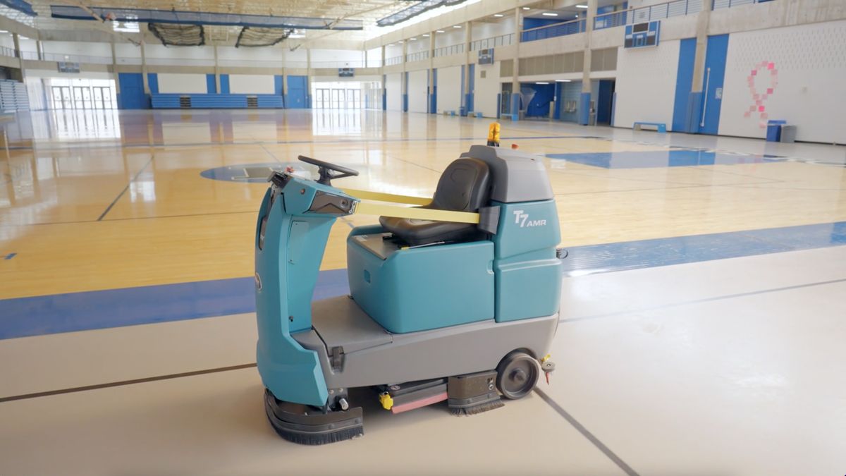 A robot floor scrubber cleans an empty basketball court.