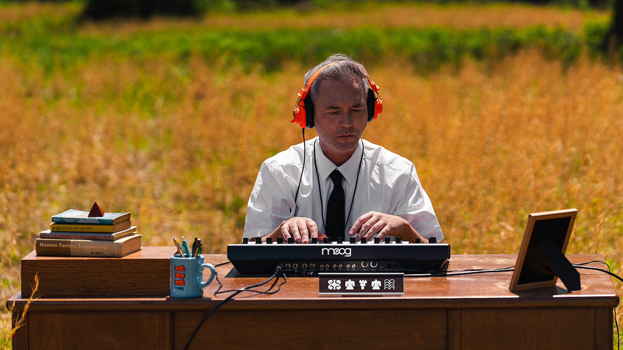 Man playing a moog at a desk in a field