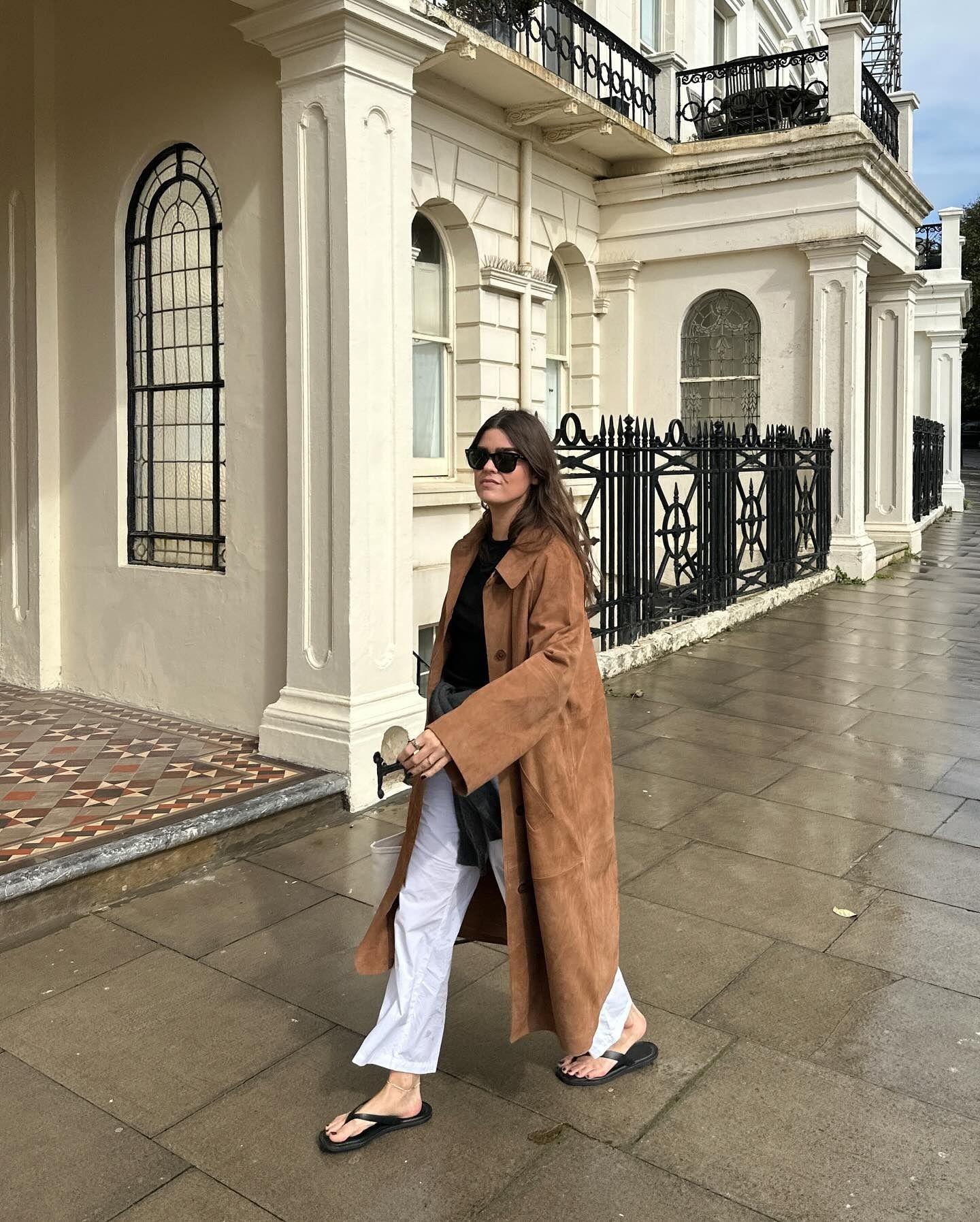 Anna Newton wearing a brown suede trench coat over a black shirt, white pants, and flip-flops.