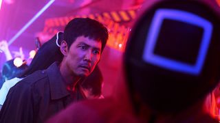 A still from the TV series Squid Game (season 2) on Netflix of Lee Jung-jae as Seong Gi-hun surrounded by neon lights.