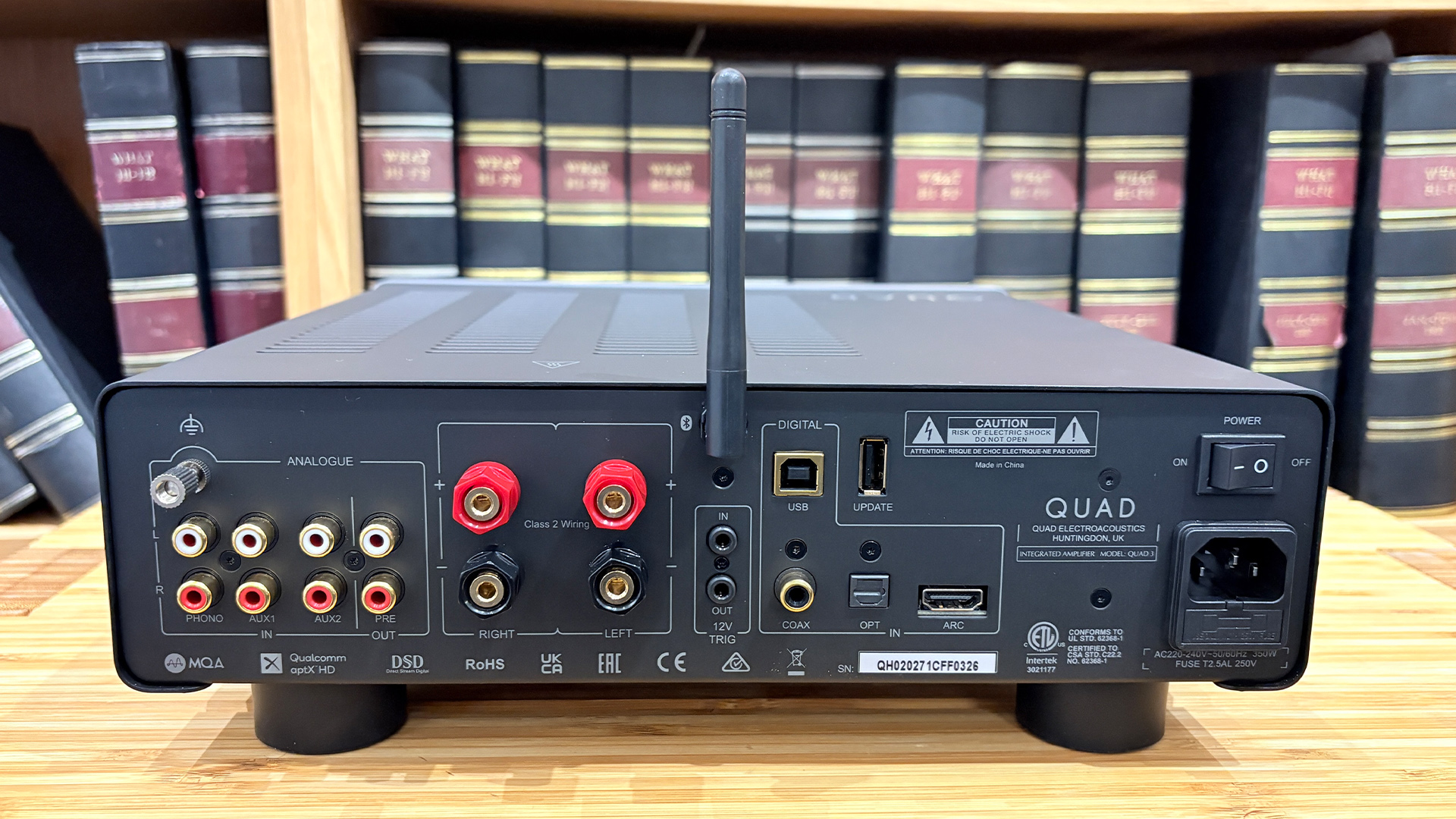 Quad 3 integrated amplifier on wooden hi-fi rack in front of bookcase, rear of unit showing connections