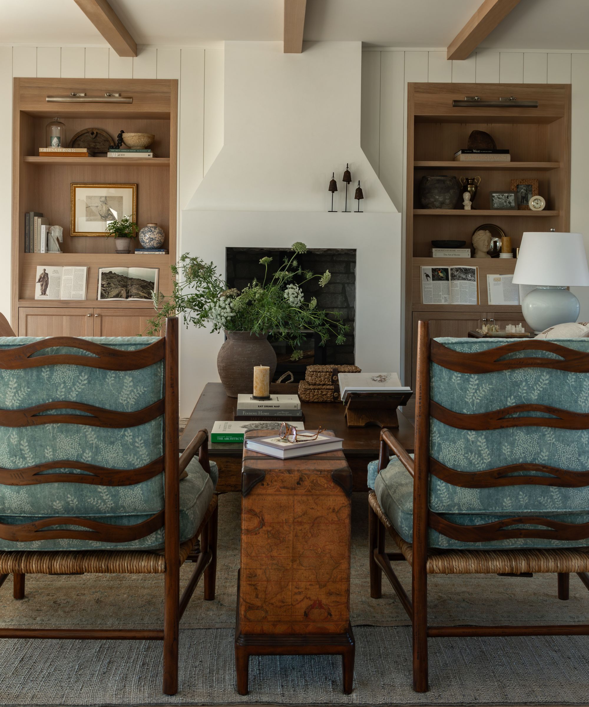 cottage style living room by Oho Interiors with a white fireplace, oak alcove bookcases, two antique chairs with blue cushions and a vintage burl side table