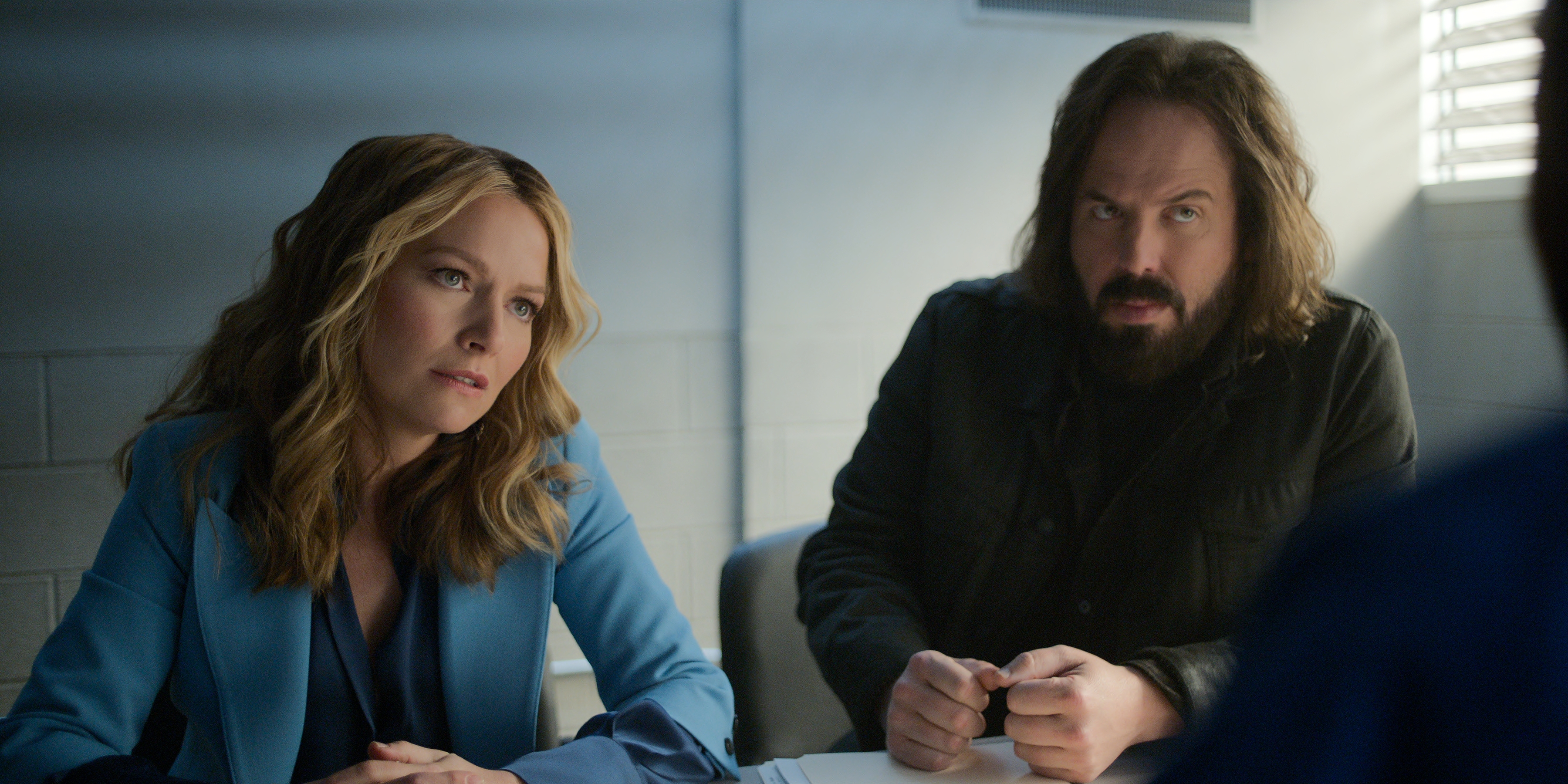 Becki Newton as Lorna Crane wearing a blue blazer and Angus Sampson as Denis &quot;Cisco&quot; Wojciechowski wearing a grey blazer having a conversation across a table in episode 401 of The Lincoln Lawyer