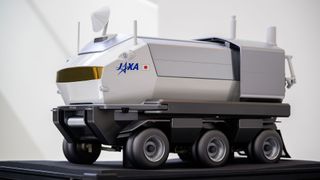 a model of a large, six-wheeled white moon rover rests on a table
