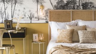 Bedroom with yellow ochre walls, a bed with rattan headboard and tropical palm print wallpaper