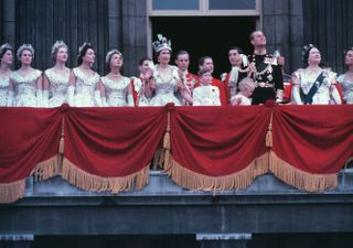 Queen Elizabeth stands on the Buckingham Palace balcony with members of the Royal Family following her Coronation, wearing the heavy Coronation Crown