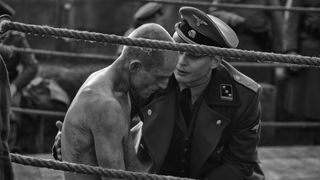 Ben Foster sits in a boxing ring with Billy Magnussen, dressed as a Nazi, speaking to him in The Survivor