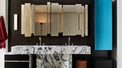 A bathroom with dark walls, a marble sink and an organic mirror design