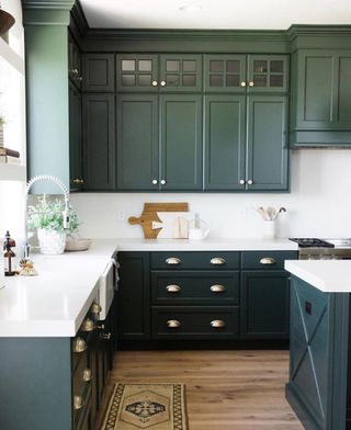 Light kitchen, with white walls and counters, dark green cabinets and wooden floors.