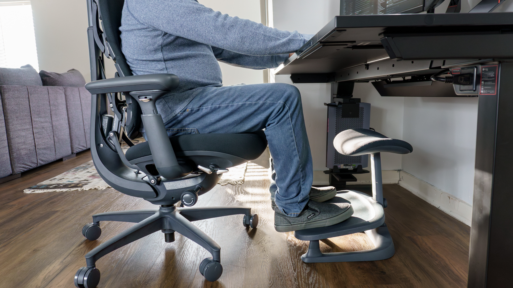 A person sitting on the LiberNovo Omni office chair with their feet up on the LiberNovo StepSync footrest in front of a desk