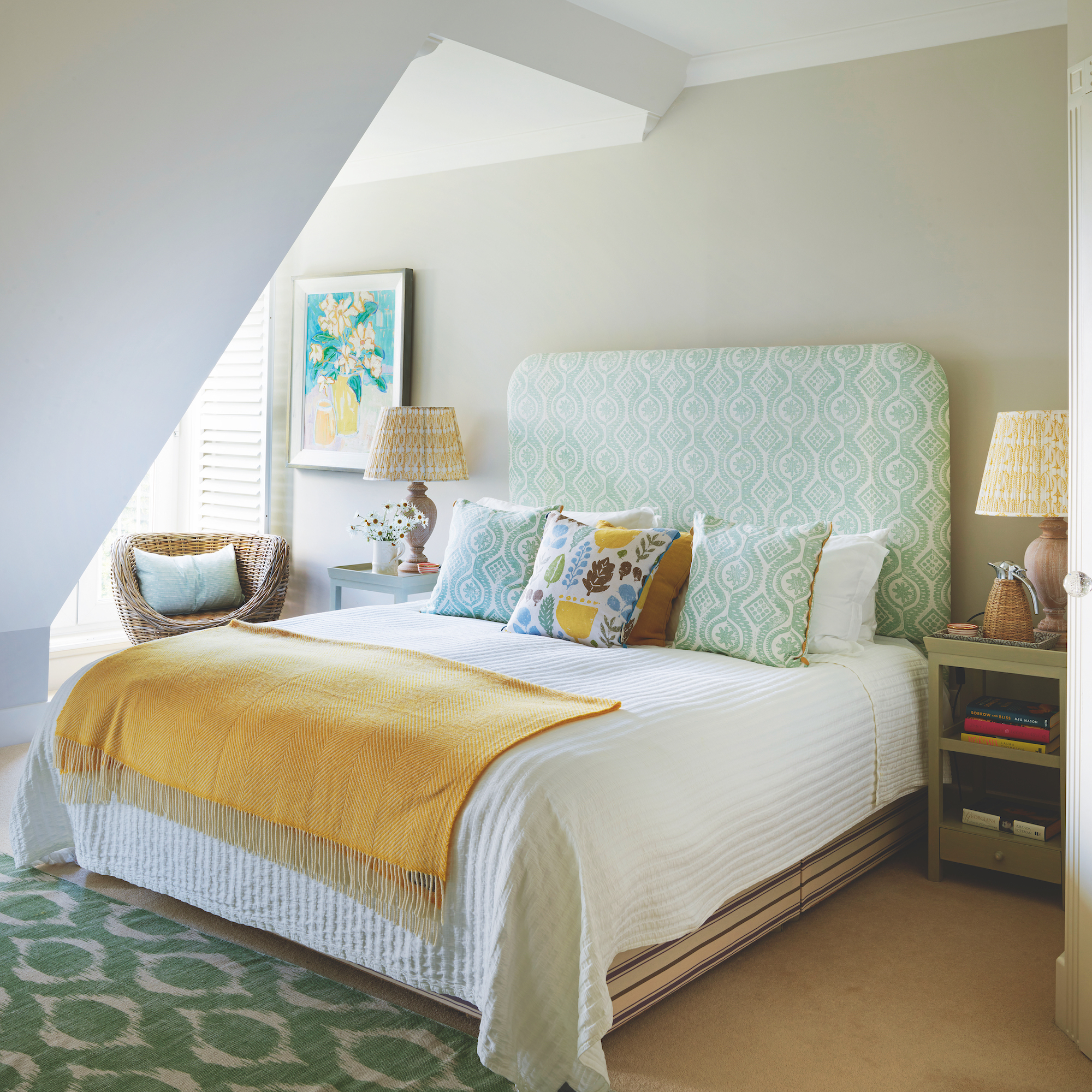 pale green bedroom with green upholstered headboard and bed with yellow throw, green rug on floor