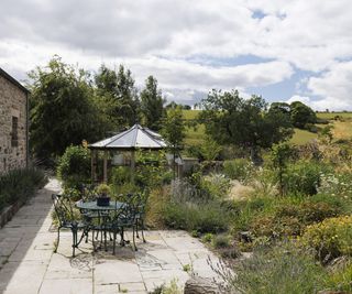 A stone paved patio with large abundant planting beds with views out to the hillside