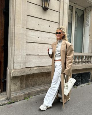 woman in white jeans, sneakers, coat, and sweater