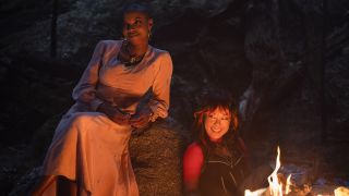 Jennifer and Alice smile as they sit by a campfire in Agatha All Along