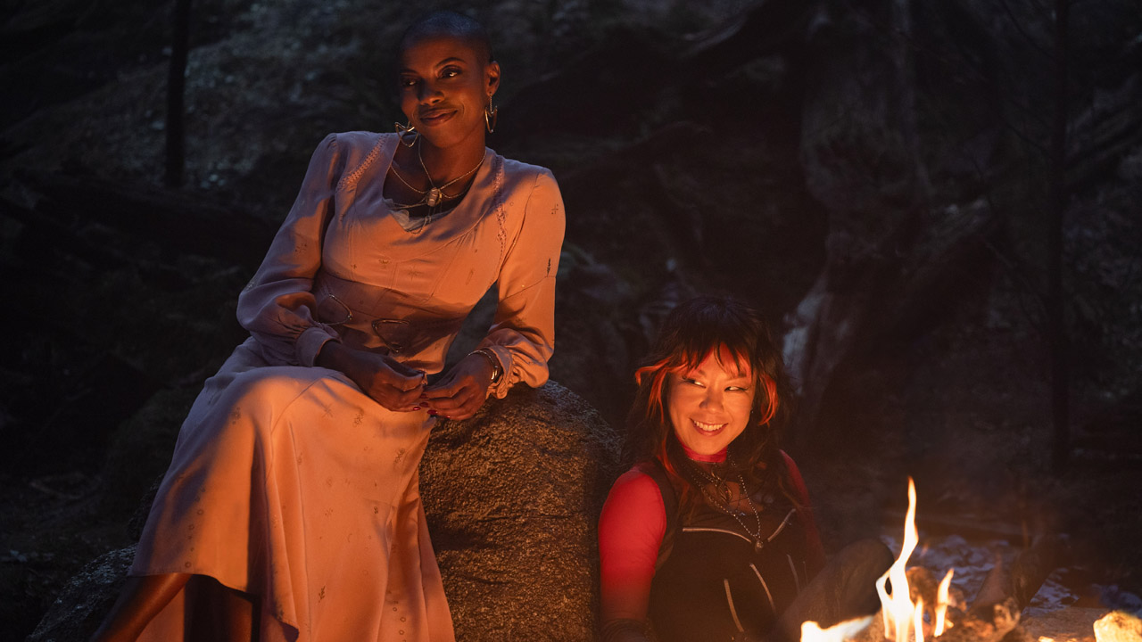 Jennifer and Alice smile as they sit by a campfire in Agatha All Along