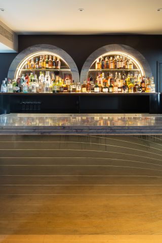 Close up of the bar at the Groucho Club with dark walls, lit arched shelving and bottles of drinks