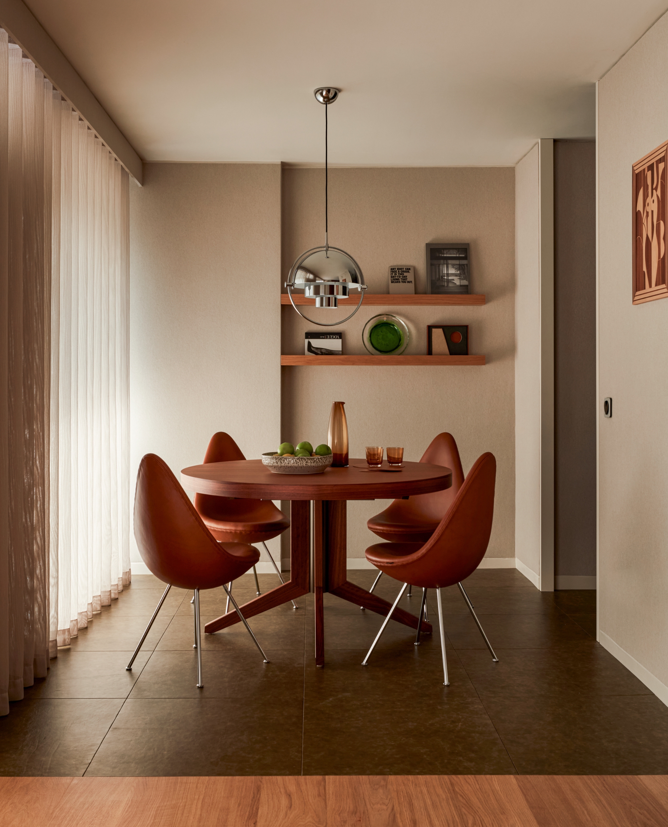 Modern dining area with red leather chairs, olive green tiles and red wood, circular dining table with polished metal pendant light above.
