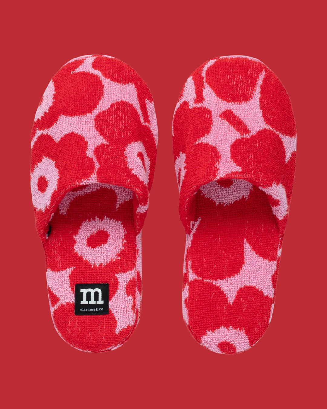 Mini Unikko Slippers in Pink against red background.
