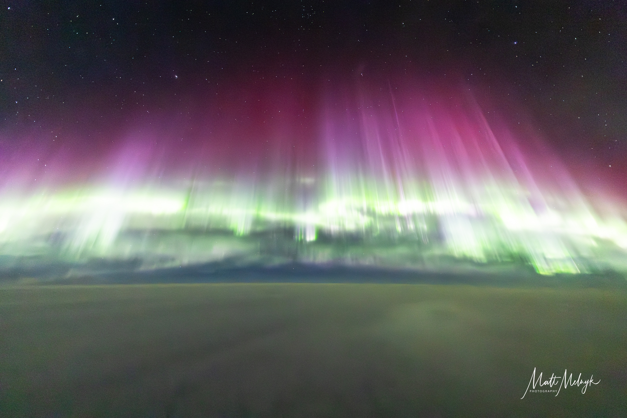 curtains of green and rich magenta auroras fill the sky, with a blanket of cloud below.