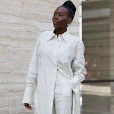 a photo of one of the best shirtdress outfit ideas with a woman wearing a white striped maxi over matching trousers with silver shell earrings