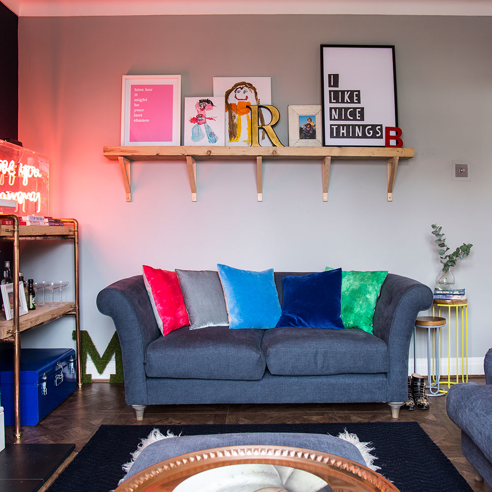 navy blue sofa with colorful pillows wall mounted shelf with painted pictures