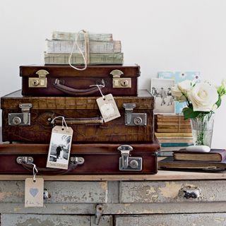 Three vintage suitcases stacked on a sideboard next to a vase of roses