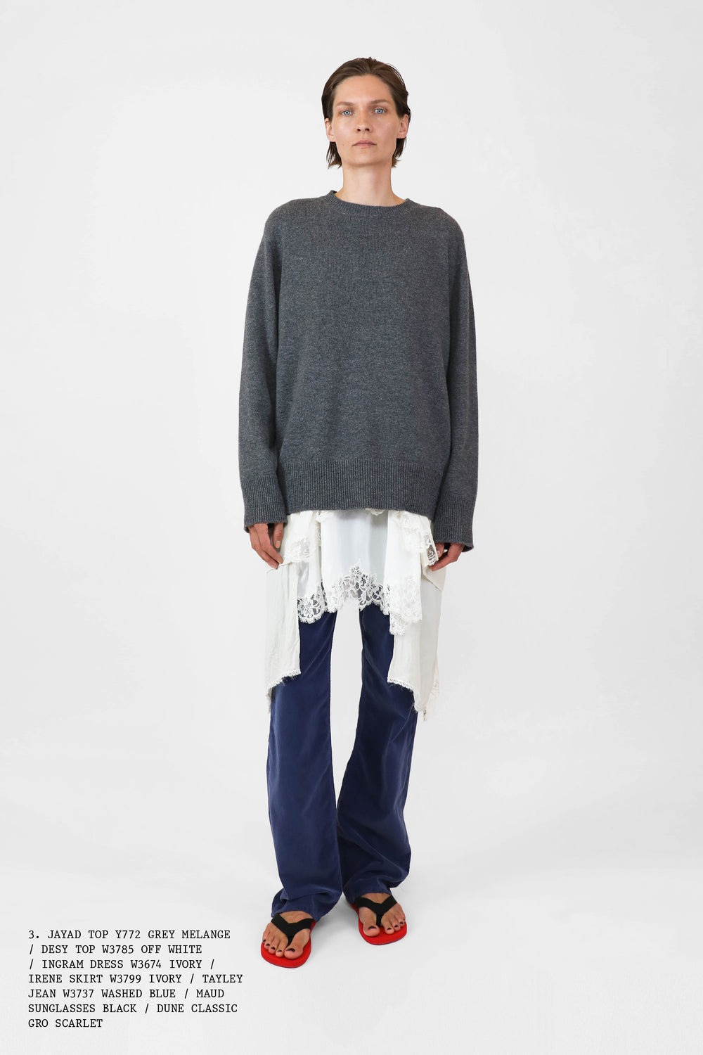 A The Row model from the spring 2025 lookbook wearing a gray sweater, white lace-trim dress, blue pants, and red flip flops.