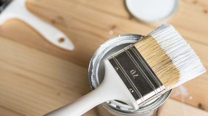 A tin of white primer with a paint brush resting on top