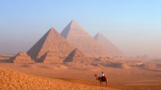 A Bedouin on a camel by the Pyramids of Khafre and Menkaure at the Giza Necropolis in Egypt.