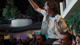 A boy is lifted up by two others in front of a crowd of screaming teenagers