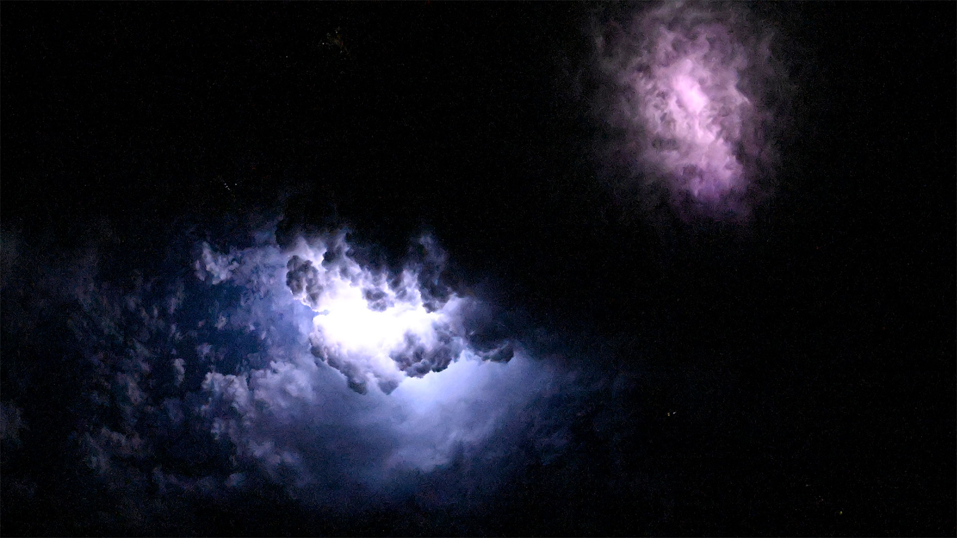 clouds are lit up at night by lightning strikes, as seen from above the planet