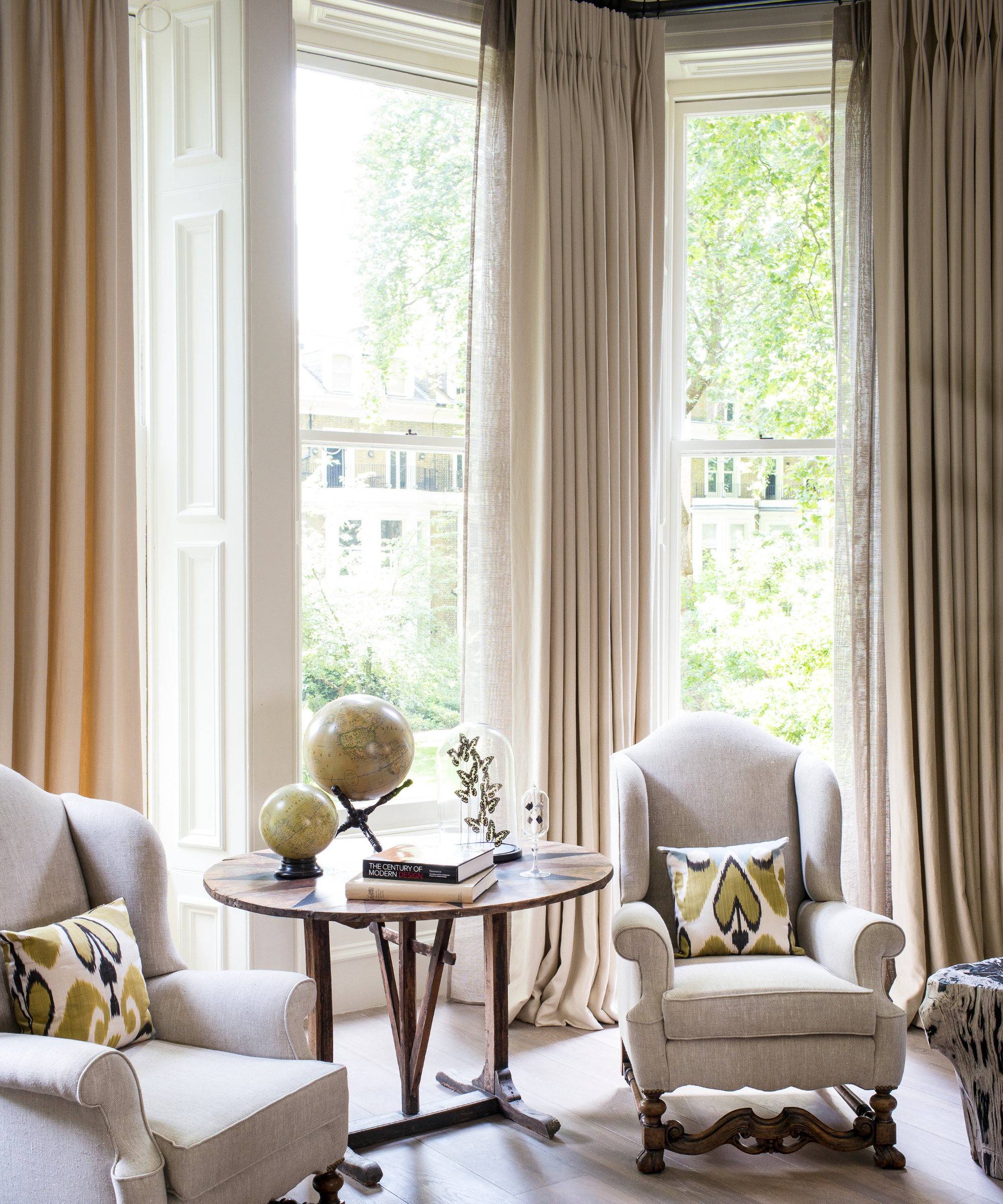 a sitting area with two chairs, a table, and tall windows with curtains
