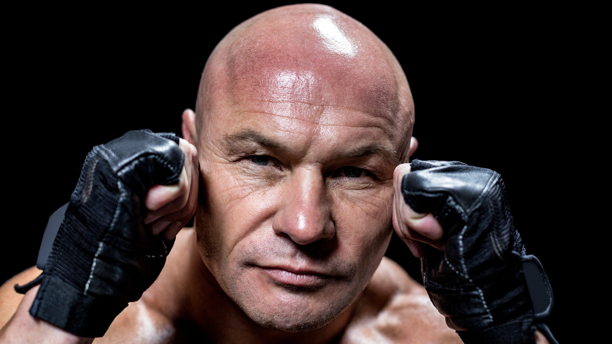 A bald-headed MMA fighter in a fighting stance with hands raised.