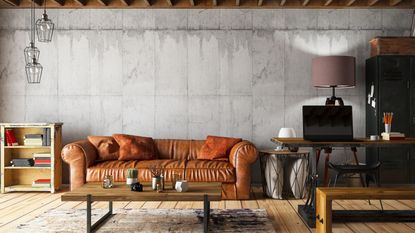 An image of a brown leather couch up against a neutral wall with a bookshelf, coffee table and desk beside it.