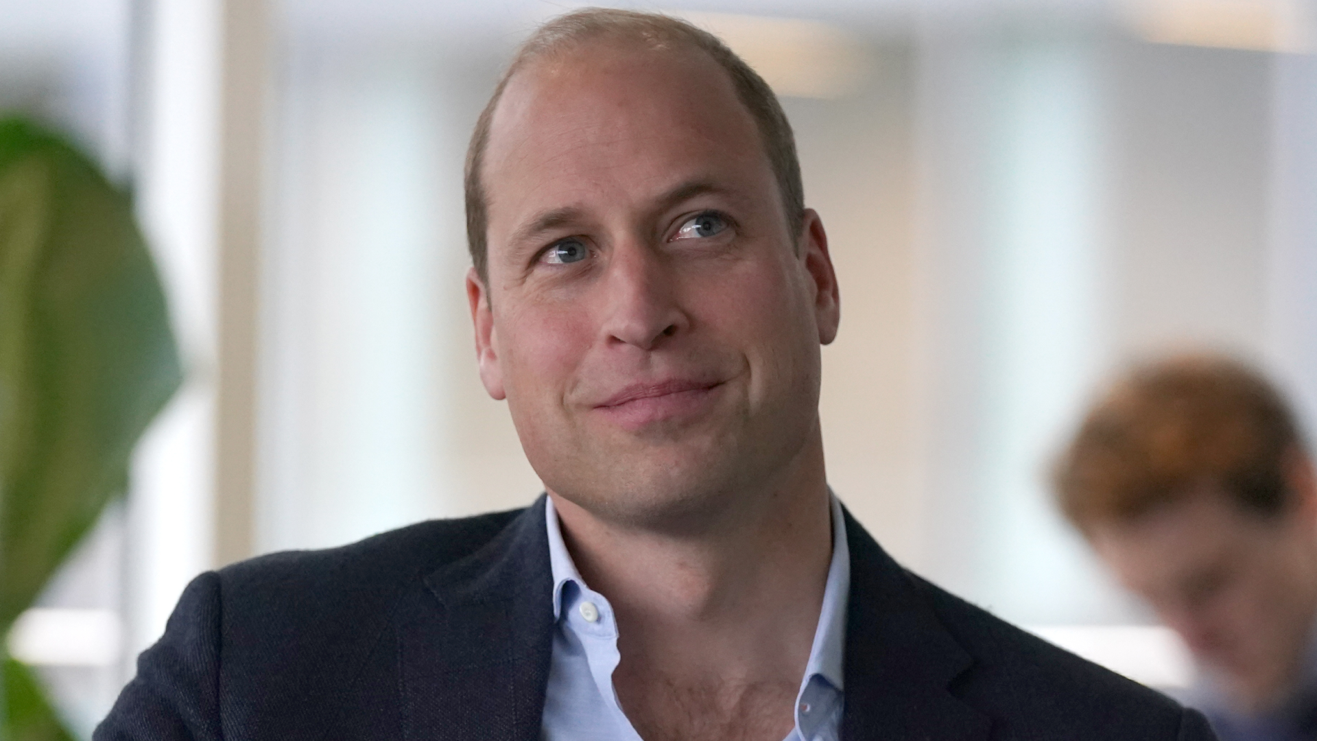 Prince William wears a navy suit and a light blue shirt and smiles awkwardly