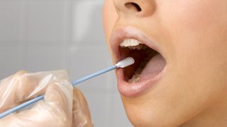 A doctor wearing clear gloves swabs the inside of a woman&#039;s cheek with a long q-tip