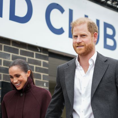 Prince Harry and Meghan Markle walking in front of a large sign on a building that says CLUB
