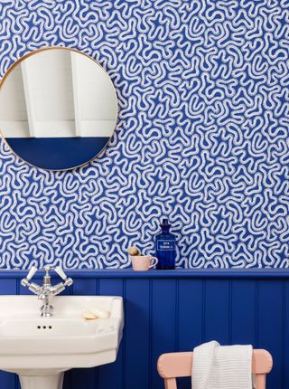 Blue bathroom wall paneling with abstract feature printed wallpaper and salmon pink accessories