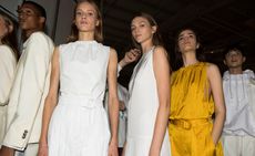 Models wear white and yellow dresses with waist belts and cream suit