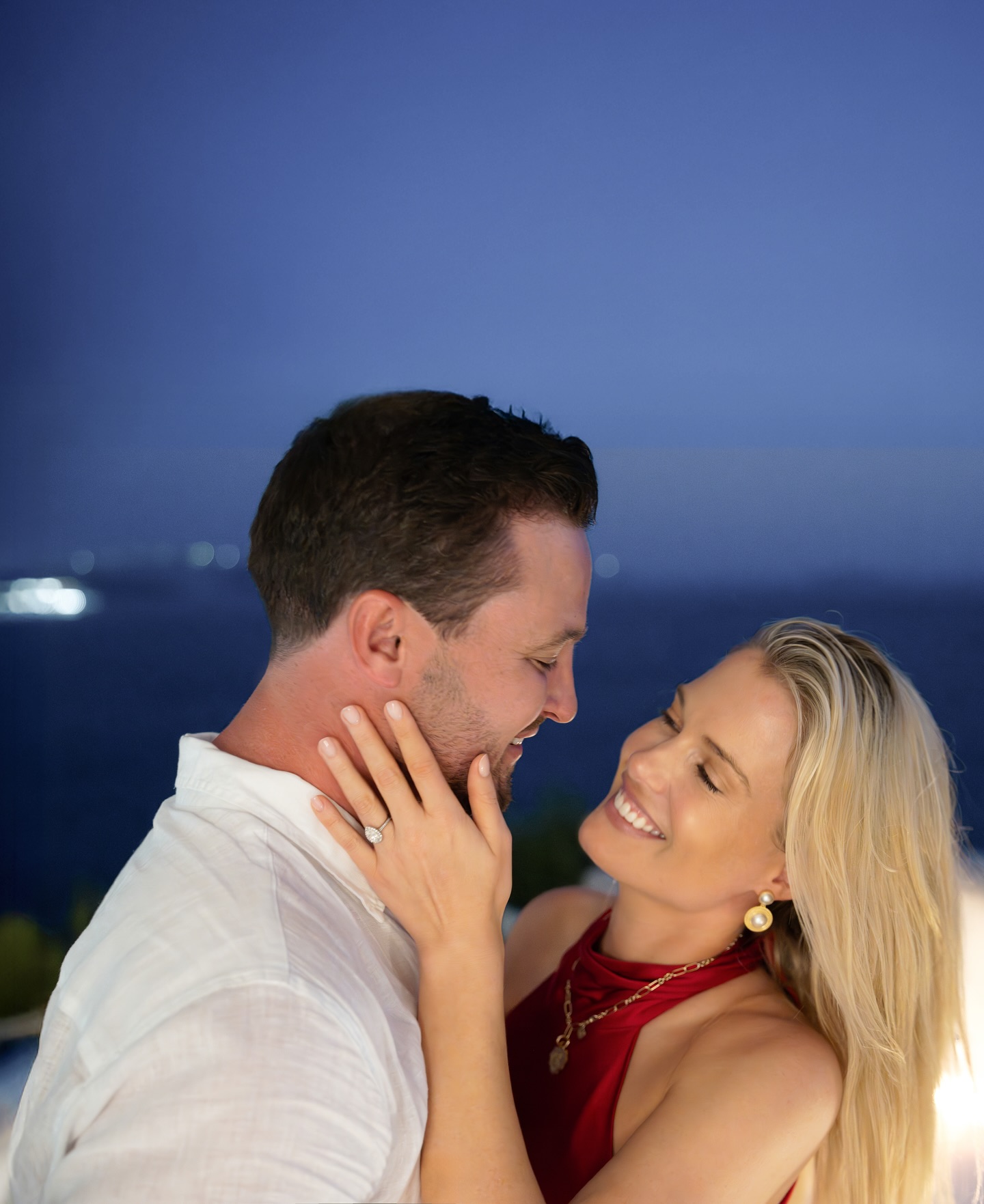 Eliza Spencer wearing a red top smiling and putting her hand on her fiance's face to show her ring