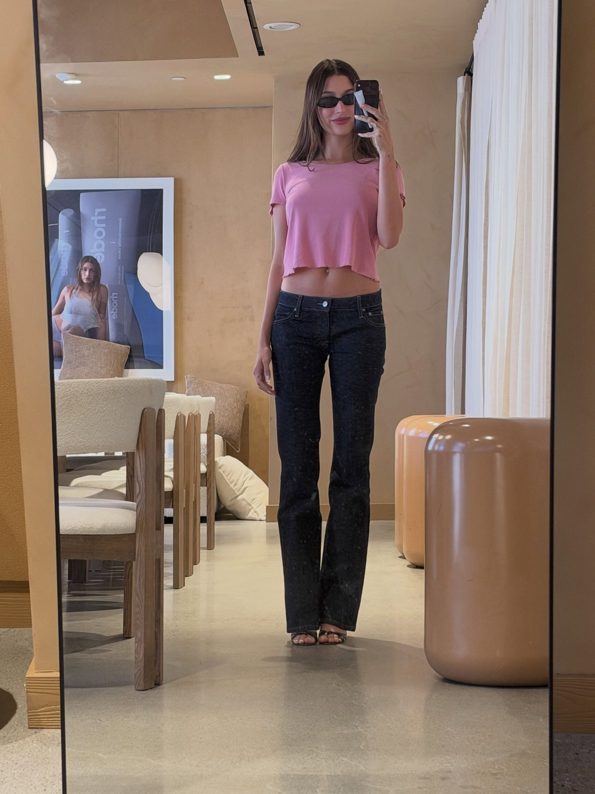 hailey wears a pink cropped tee, low-rise dark-wash bootcut jeans and open-toe heels.