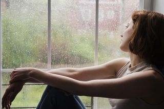 Caucasian woman sitting near rainy window daydreaming