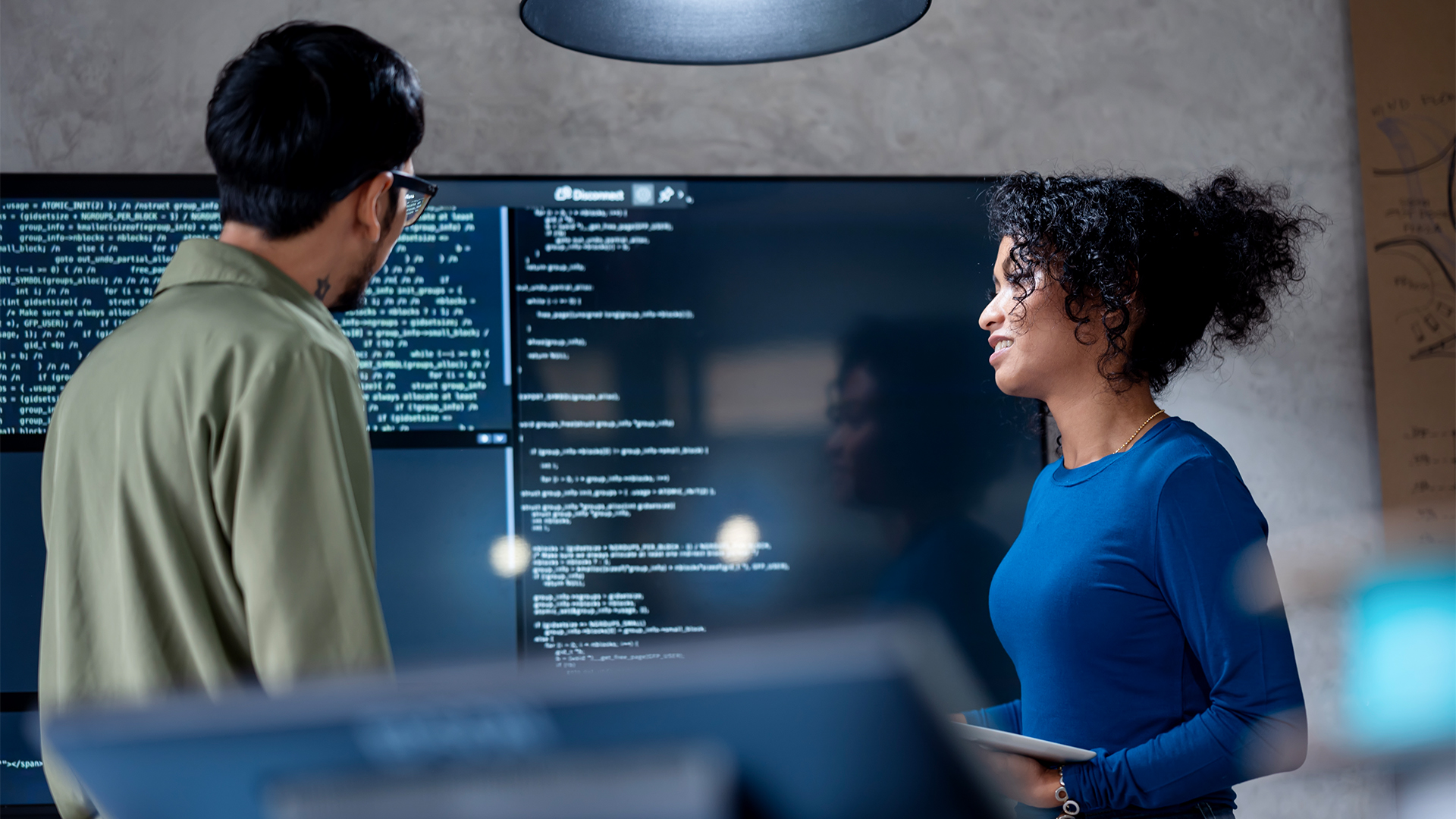 Male and female IT leaders discussing data strategy in an open plan office space while observing source code on a screen.