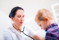 A doctor listens to a little boy's heart beat with her stethoscope