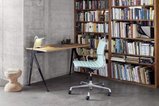 A light blue, high back, office chair photographed in a lifestyle setting. It sits next to a desk, with a bookshelf filled with books behind it.