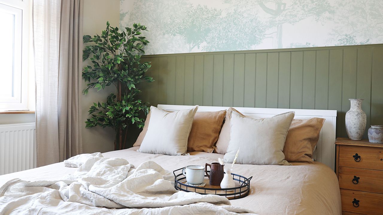 A bed with cream bedding in a bedroom with green wall panelling