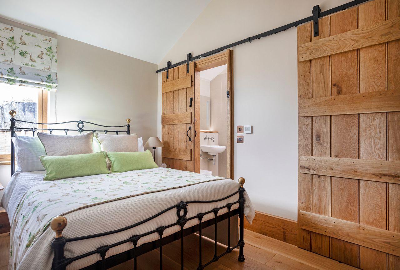 A barn conversion bedroom with a pitched ceiling and a sliding barn door leading into an ensuite