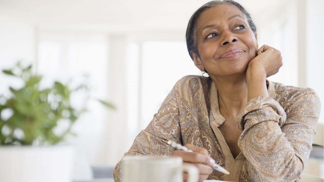 A woman smiles as she rests her chin in her palm and looks into the distance, clearly thinking.